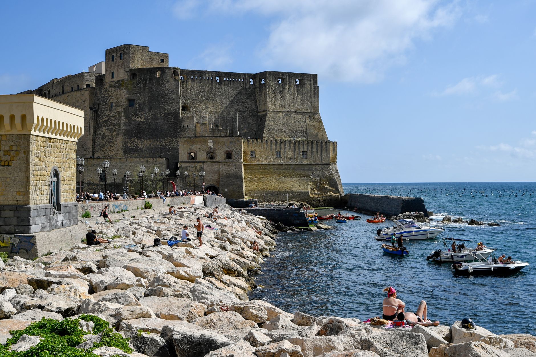 A vibrant scene of Castel dell'Ovo and its bustling seaside, capturing boats and beachgoers in Naples, Italy.